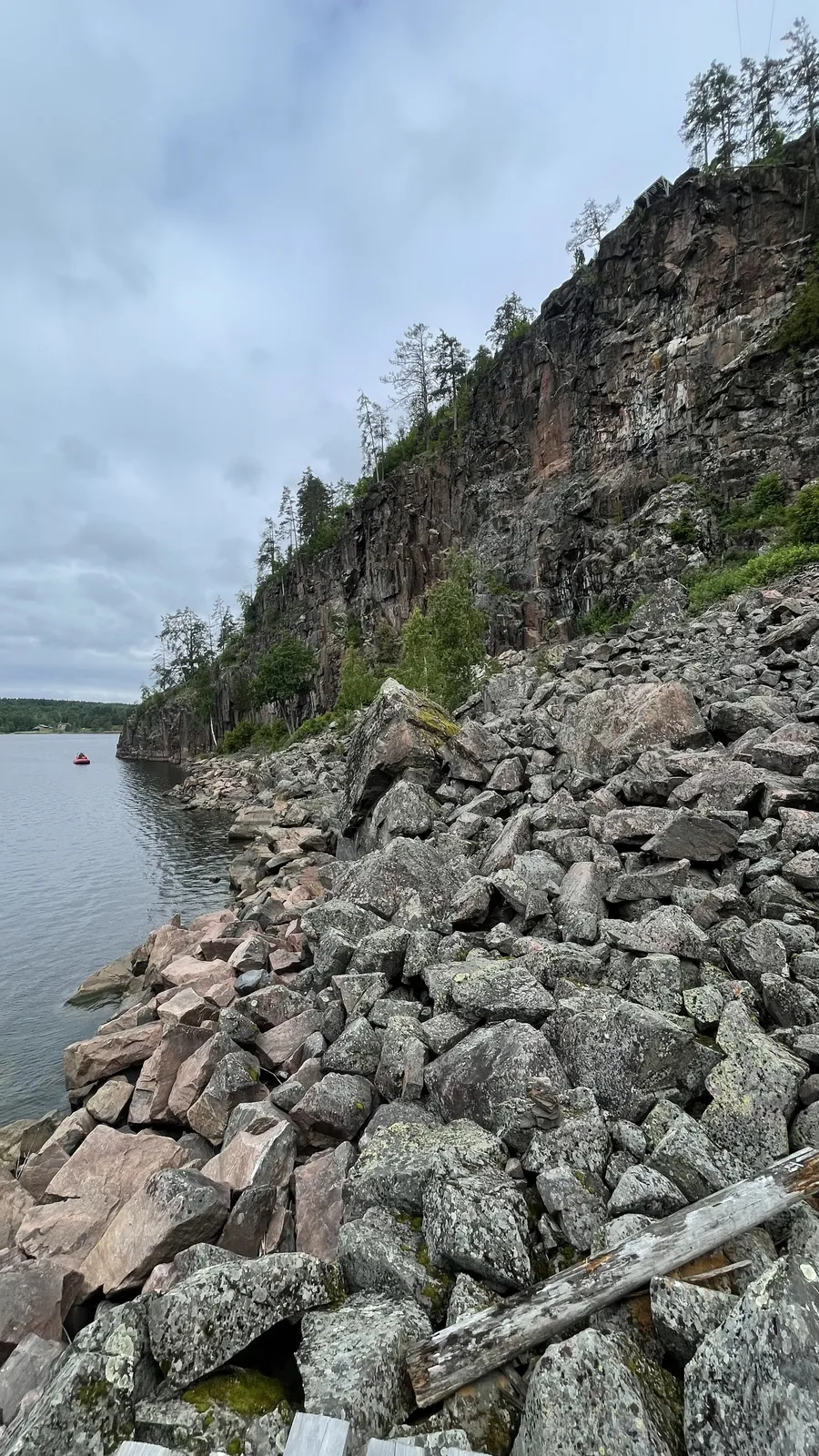 Отвесная скала над озером, каменная осыпь у воды, вдали красная лодка